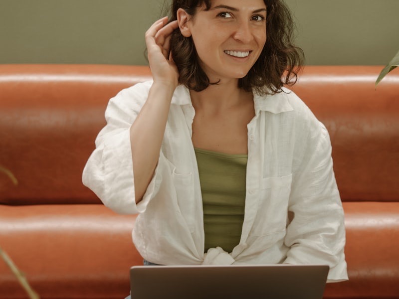 A young woman with a mug and laptop on a sofa during a video session