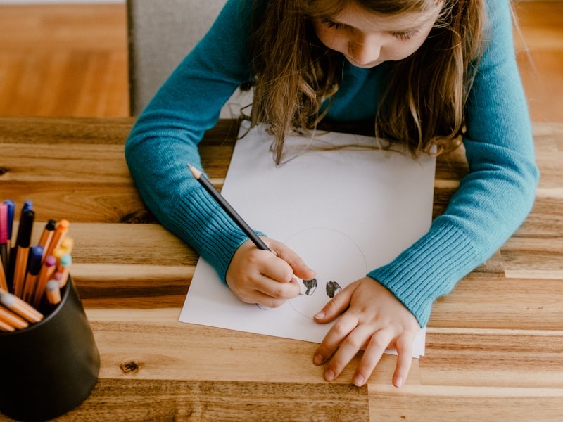 A young child drawing with colored pencils at a warm wood table