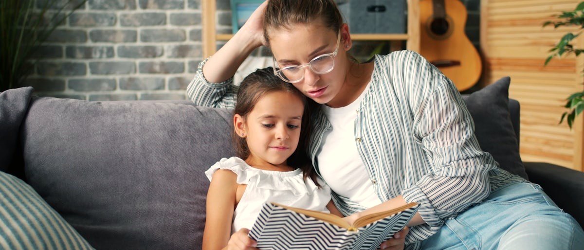 A mother and her daughter reading a book together on a sofa